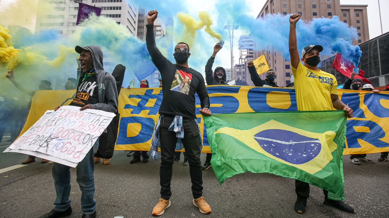 تظاهرکنندگان با ماسک صورت در خیابان پائولیستا در جریان اعتراضی که در بحبوحه همه‌گیری ویروس کرونا (COVID-19) در 14 ژوئن 2020 در سائوپائولو، برزیل برگزار شد، مشت‌های خود را بالا می‌برند.